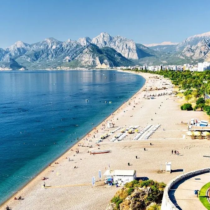 Scenic beach with mountains in the background and clear blue water.