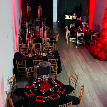 Elegant event setup with black and red decor and gold chairs.