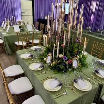 Elegant banquet table with green linens, gold cutlery, and tall candle centerpiece.
