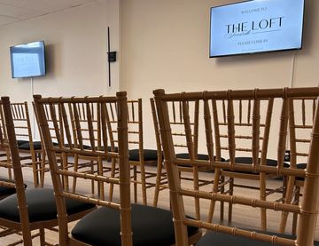 Empty wooden chairs facing screens in a minimalist event space.