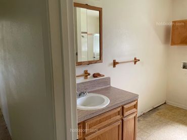 Looking into empty bathroom with vanity, cabinet, towel rack, and washer outlet.