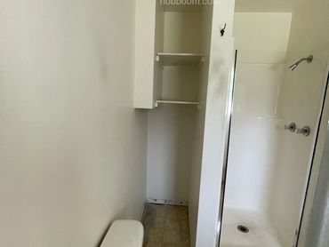 A view in a narrow bathroom showing a shower and shelves