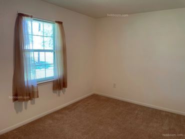 View of the corner of an empty bedroom with window and curtains