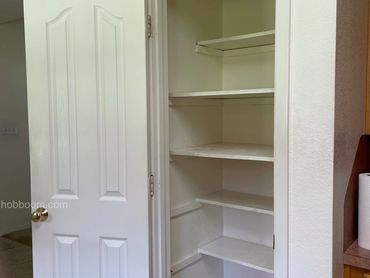 View of empty white pantry shelves and soor.
