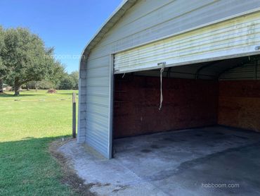 Look at half-open roll-up door to a metal shop building with concrete slab.