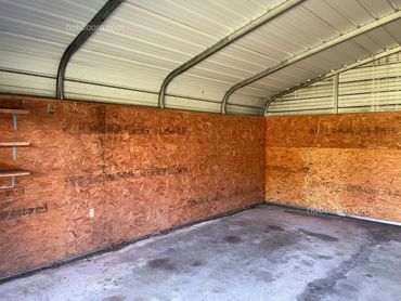 Inside metal shop building with shelves on the chipboard wall.