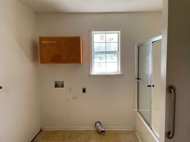 An empty bathroom with window, cabinet, and shower