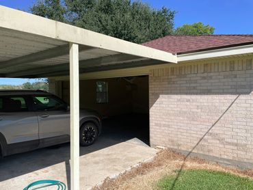A view of the outside carport, support post, and a grey car.