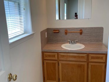 A bathroom sink, mirror and cabinets with window