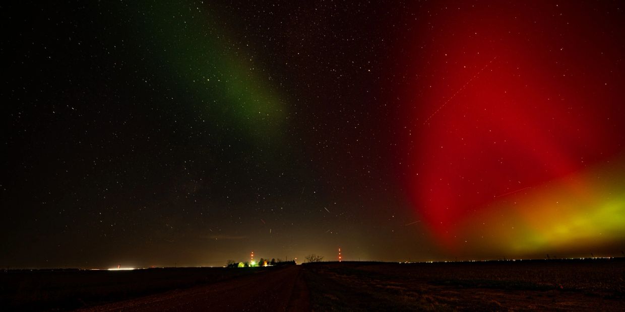 Night sky with vibrant red and green northern lights over a rural landscape.