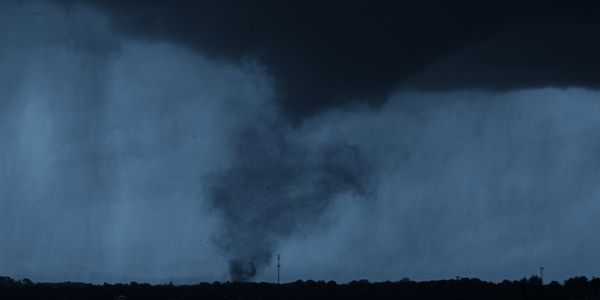 A dark tornado funnel touching down on the horizon under stormy skies.