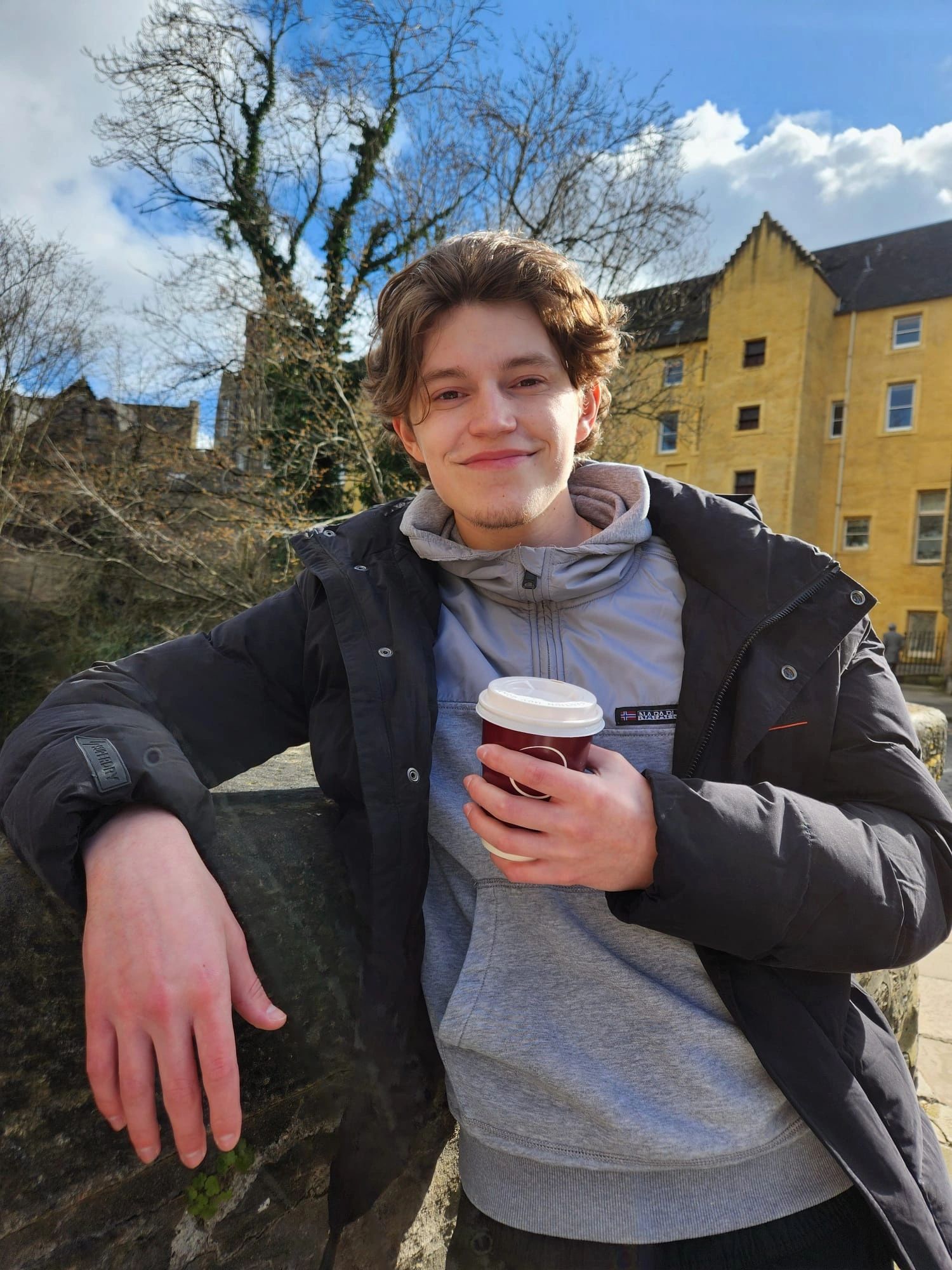 Young man enjoying a sunny day outdoors with a warm drink.