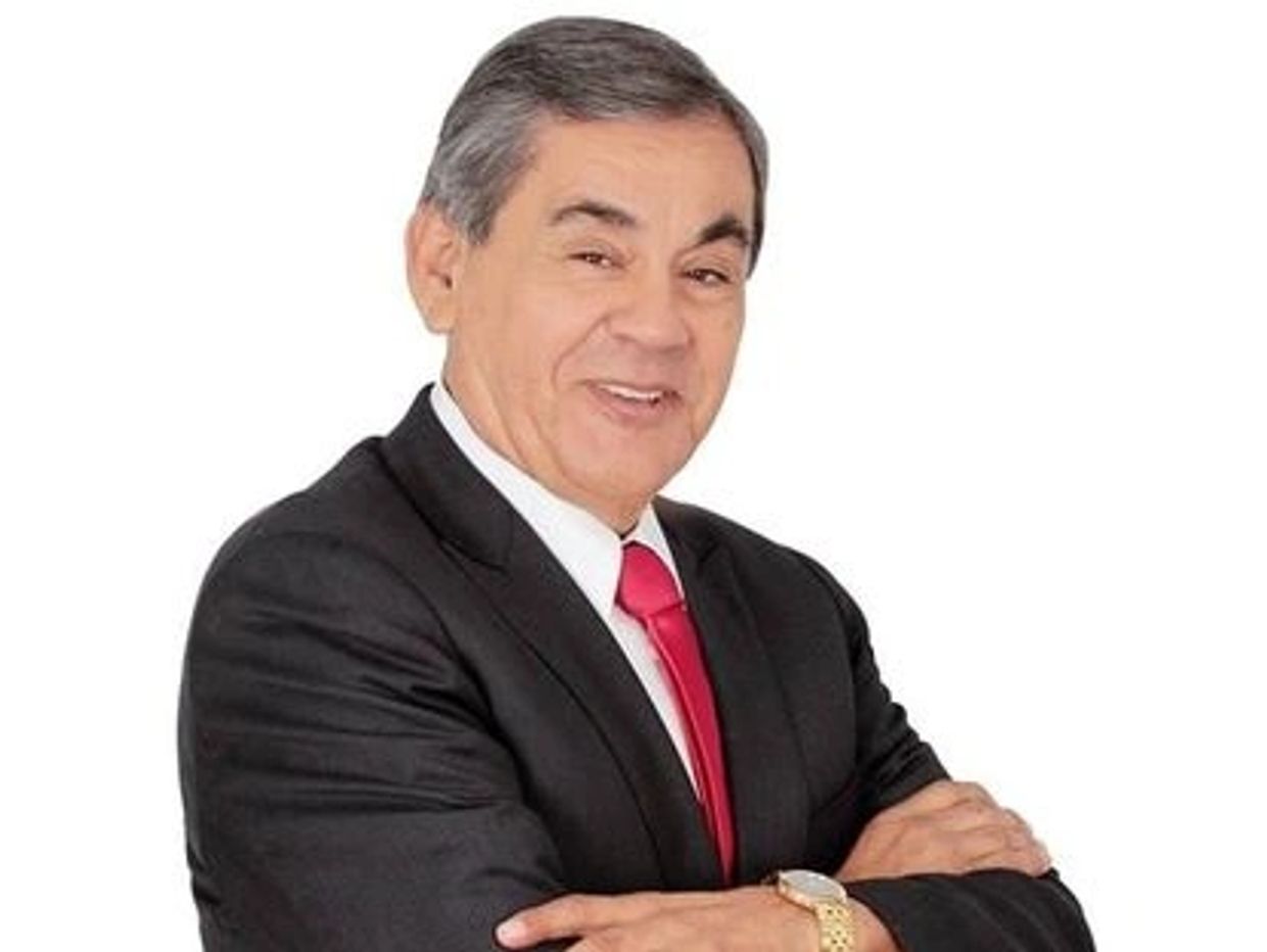 Hombre con traje negro y corbata roja sonriendo.