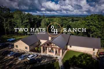 Aerial view of Two Hats Ranch building surrounded by trees under a cloudy sky.