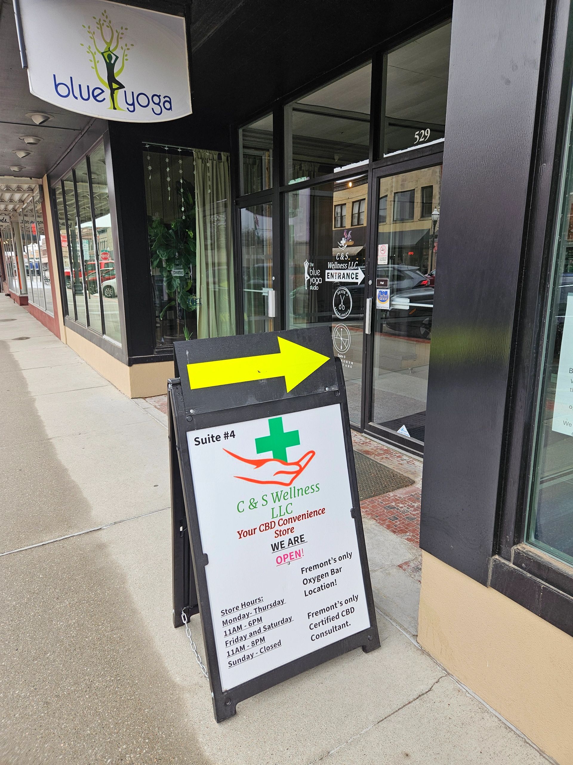Sidewalk sign directing to C & S Wellness LLC, a CBD convenience store, next to Blue Yoga studio.