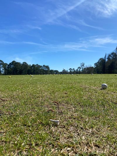 Close-up of golf ball and tee on a sunny driving range.