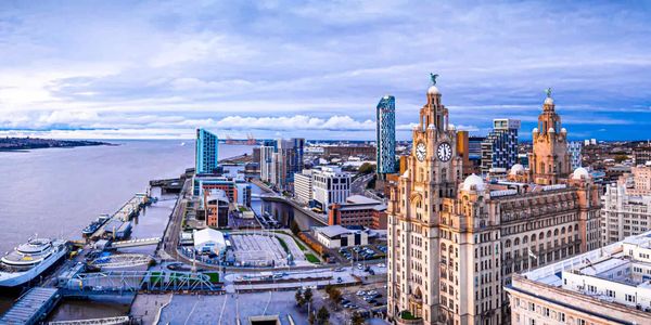 Cityscape of Liverpool with waterfront and historic buildings under a blue sky.