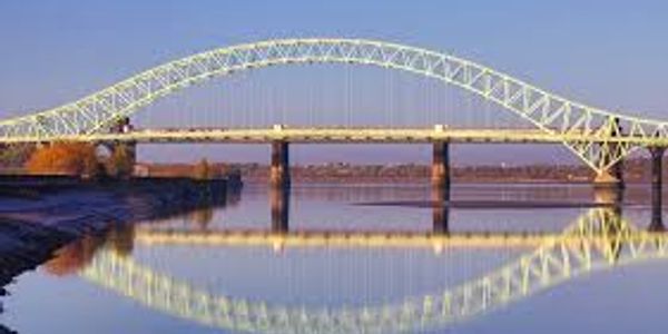 A large arch bridge reflected in calm water under a clear sky.
