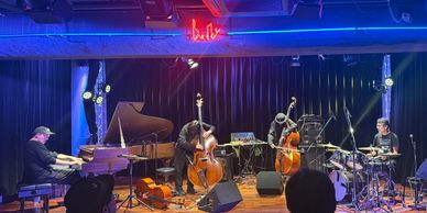 Jazz band performing live on stage with piano, double bass, cello, and drums.