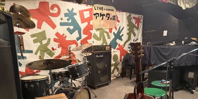A small music rehearsal room with drums, guitars, and amps.