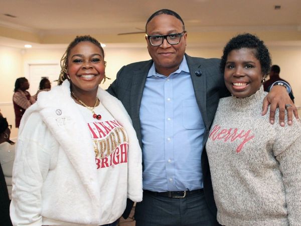 Three smiling friends posing together indoors, dressed warmly.