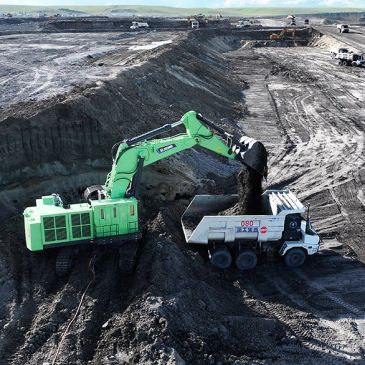 Green excavator loading dirt into a white dump truck in a mining site.
