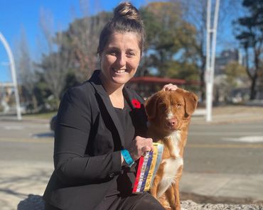 Smiling woman with a dog holding ribbons outdoors.