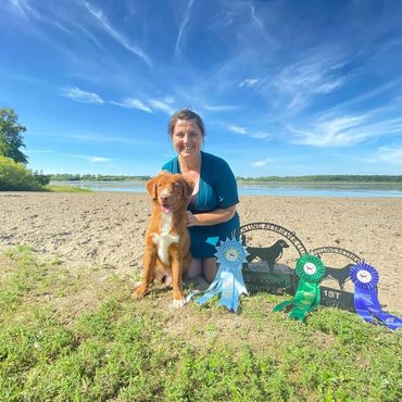 Woman with dog and award ribbons outdoors.