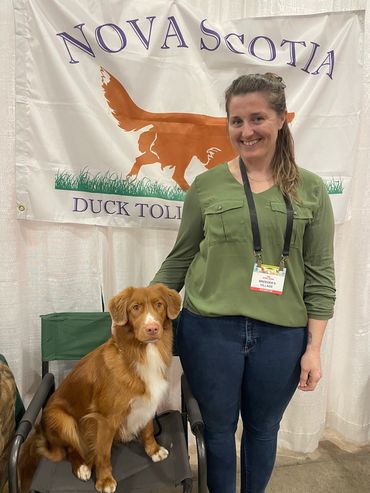 Woman posing with a dog at Nova Scotia Duck Tolling Retriever banner.
