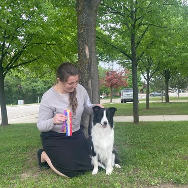 Woman with a dog and award ribbons outdoors.