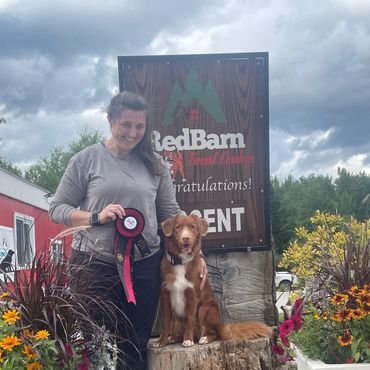 Woman and dog pose with a prize ribbon at an event.