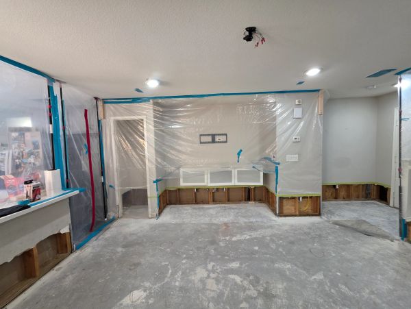 Room under renovation with plastic coverings and exposed lower walls.
