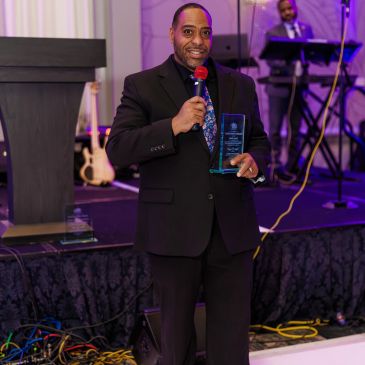 Man holding an award and microphone on stage.