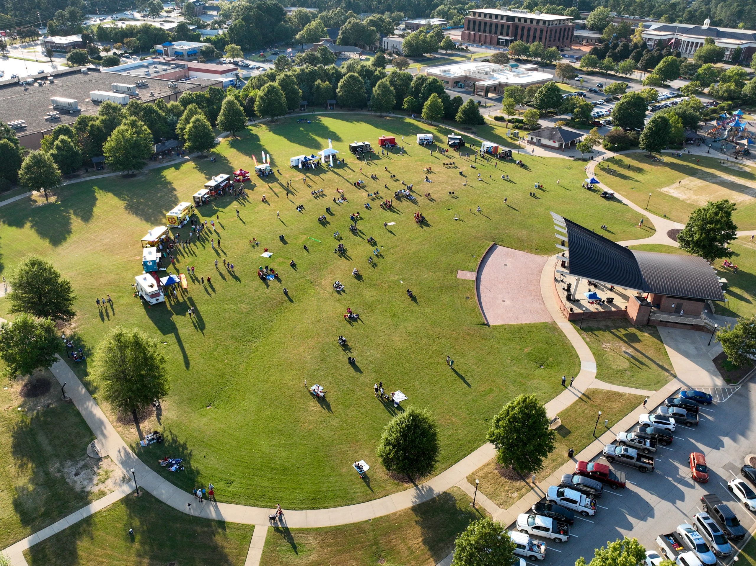 Aerial view of a park event with food trucks, people, and a stage.