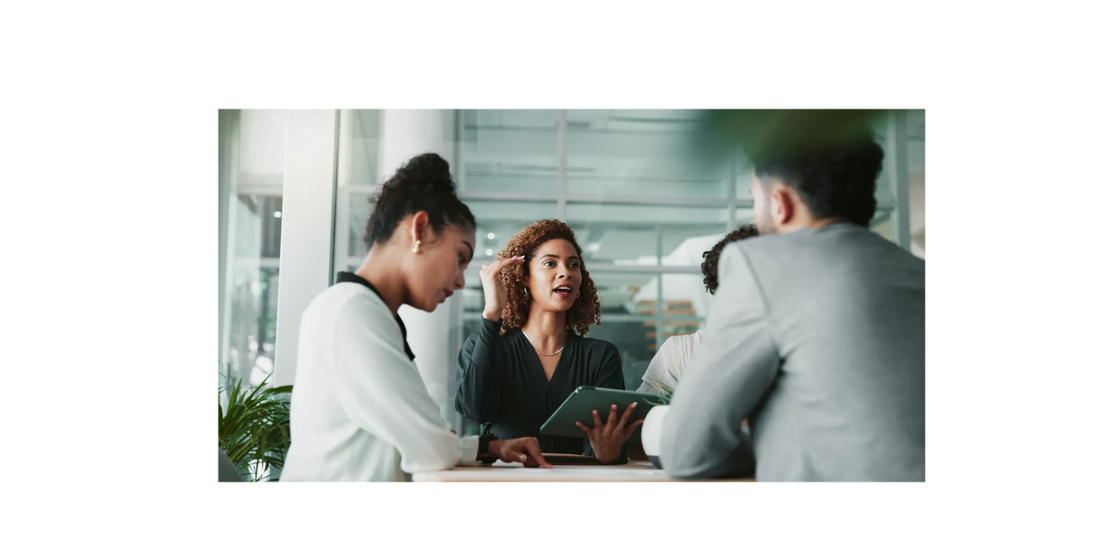 A woman holding a tablet leading a business meeting with colleagues.