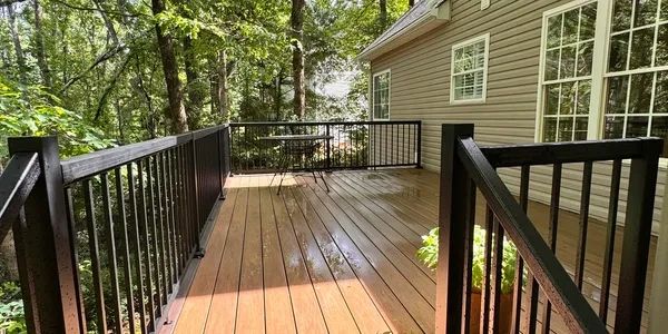 Spacious wooden deck with black metal railings attached to a house.