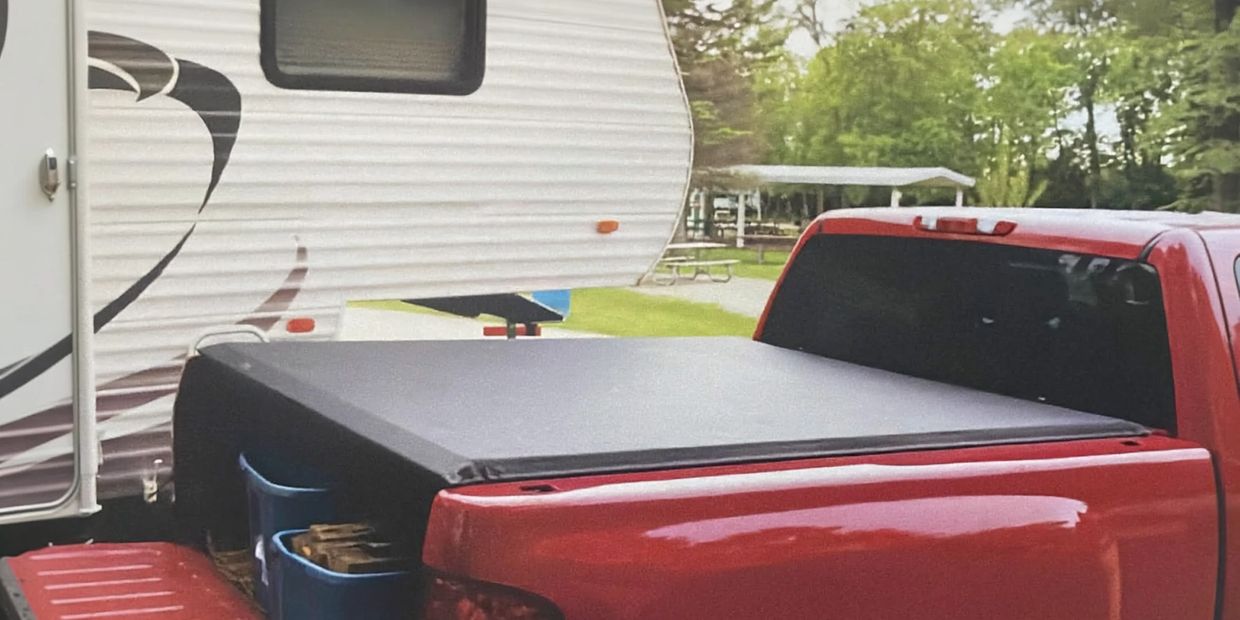 Red pickup truck with covered bed by an RV in a park.