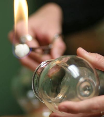 Hands holding a flame and a glass cup.