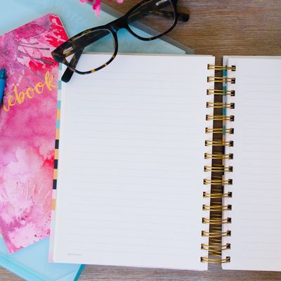 pink binder, blue pen, glasses and open notebook on a desk