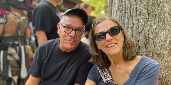 A smiling couple sitting outdoors near a tree on a sunny day.