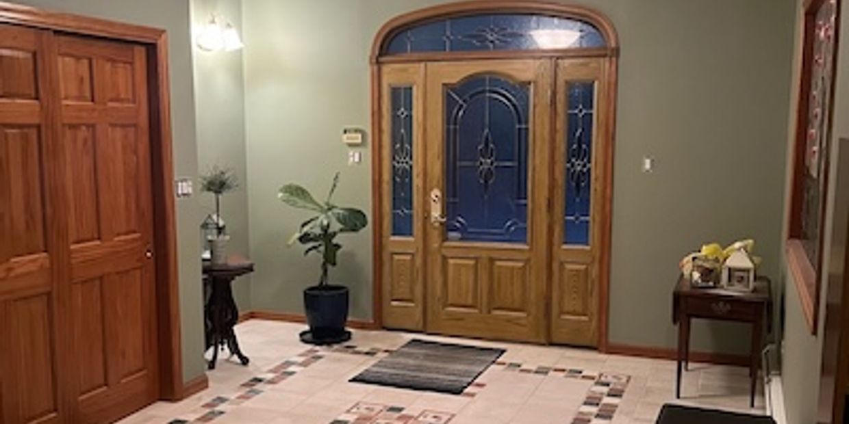 Spacious entryway with wooden door, plants, and decorative rugs.