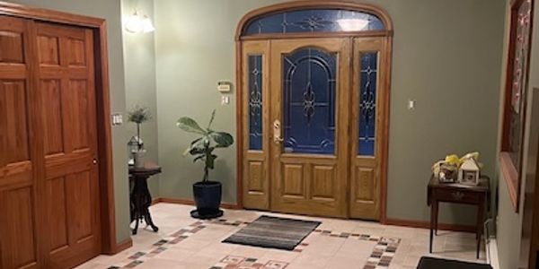 Spacious entryway with wooden door, plants, and decorative rugs.