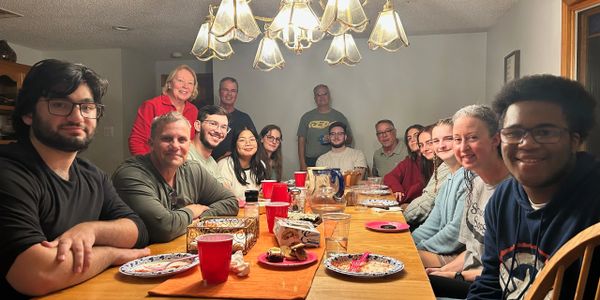 A diverse group gathered around a dinner table with smiles and empty plates.