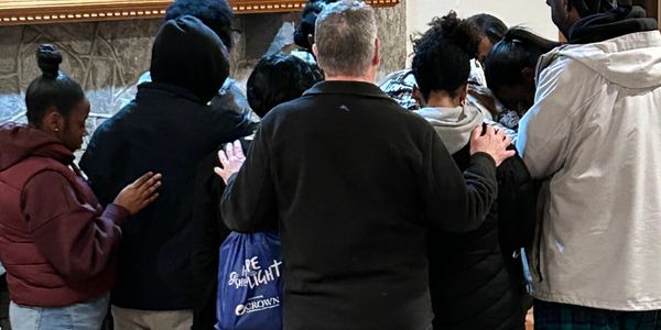 Group of people standing close in a circle with hands on each other's shoulders.