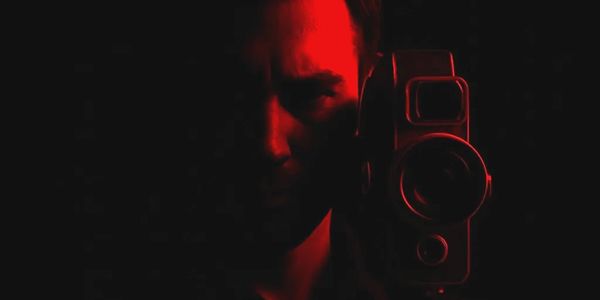 Man holding a vintage camera, illuminated in red light against a dark background.
