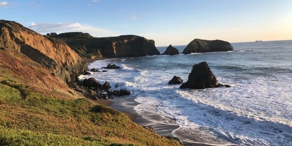 Rocky coastline with waves crashing under a clear sky at sunset.