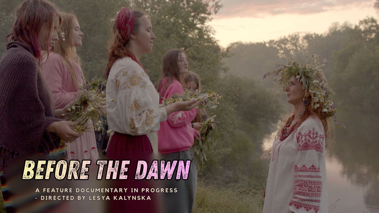 Women in traditional attire holding flowers by a riverside.