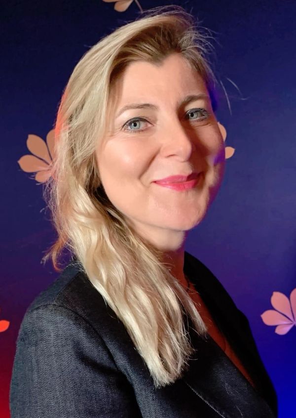 Smiling woman with blonde hair against a floral dark background.