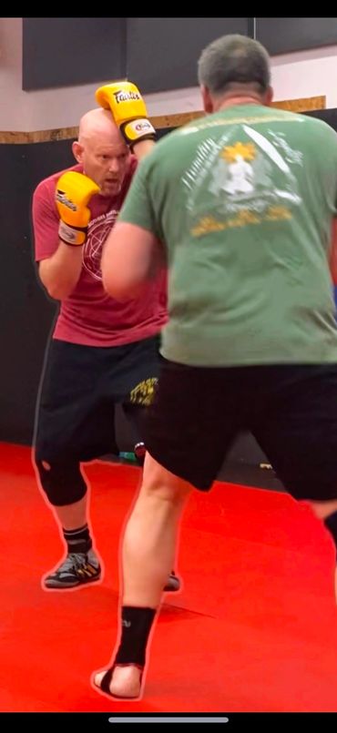 Two men sparring with yellow boxing gloves indoors.