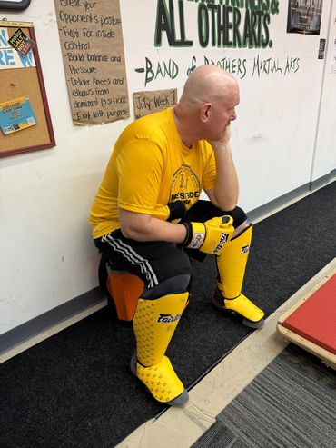 Man in yellow martial arts gear sitting against wall, resting head on hand.